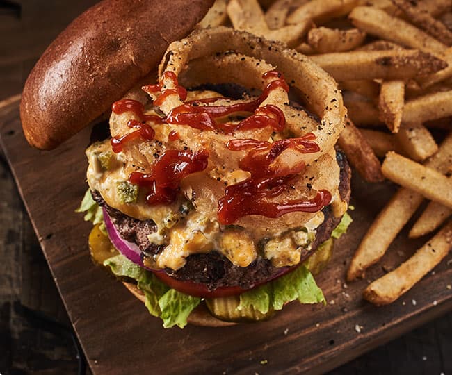 Beef burger accompanied by cheese, lettuce, tomato, pickles, red onion, Cajun sauce, mayonnaise and onion rings. Served with French fries.