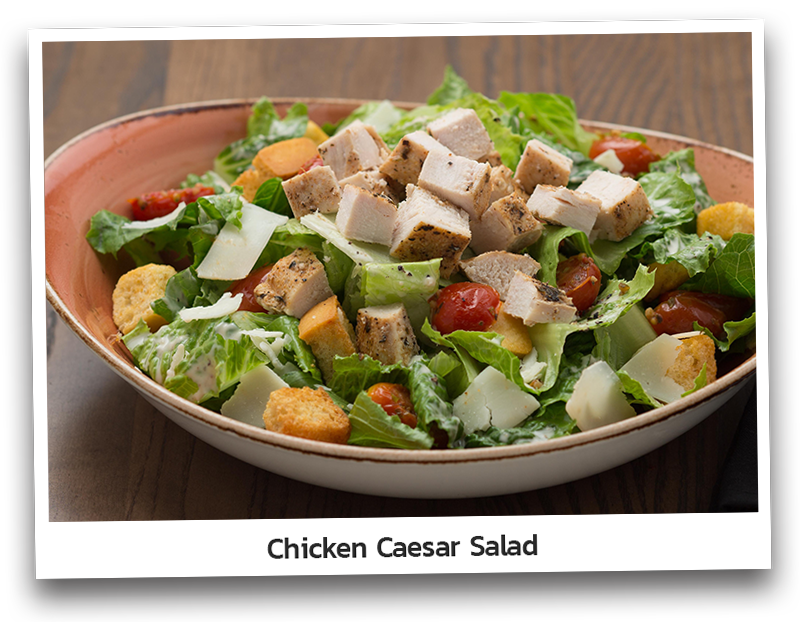 Picture the Chicken Caesar Salad which includes of roasted chicken breast served with Romaine, roasted tomatoes, croutons, Asiago cheese and Caesar dressing and presented on a round plate.