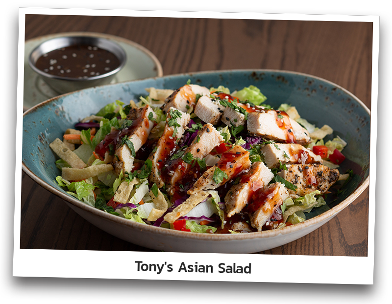 Picture the Tony’s Asian Salad that includes fresh chopped Asian greens, diced red bell pepper, cilantro, crispy wontons noodles, and sesame seeds and topped with sliced roasted chicken and drizzled with Thai Chili sauce. Served with Pan Asian dressing on a round plate.